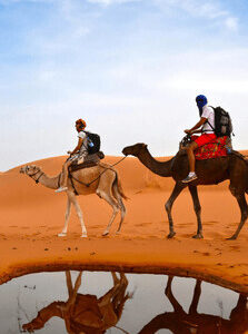 Two people riding camels in desert Morocco